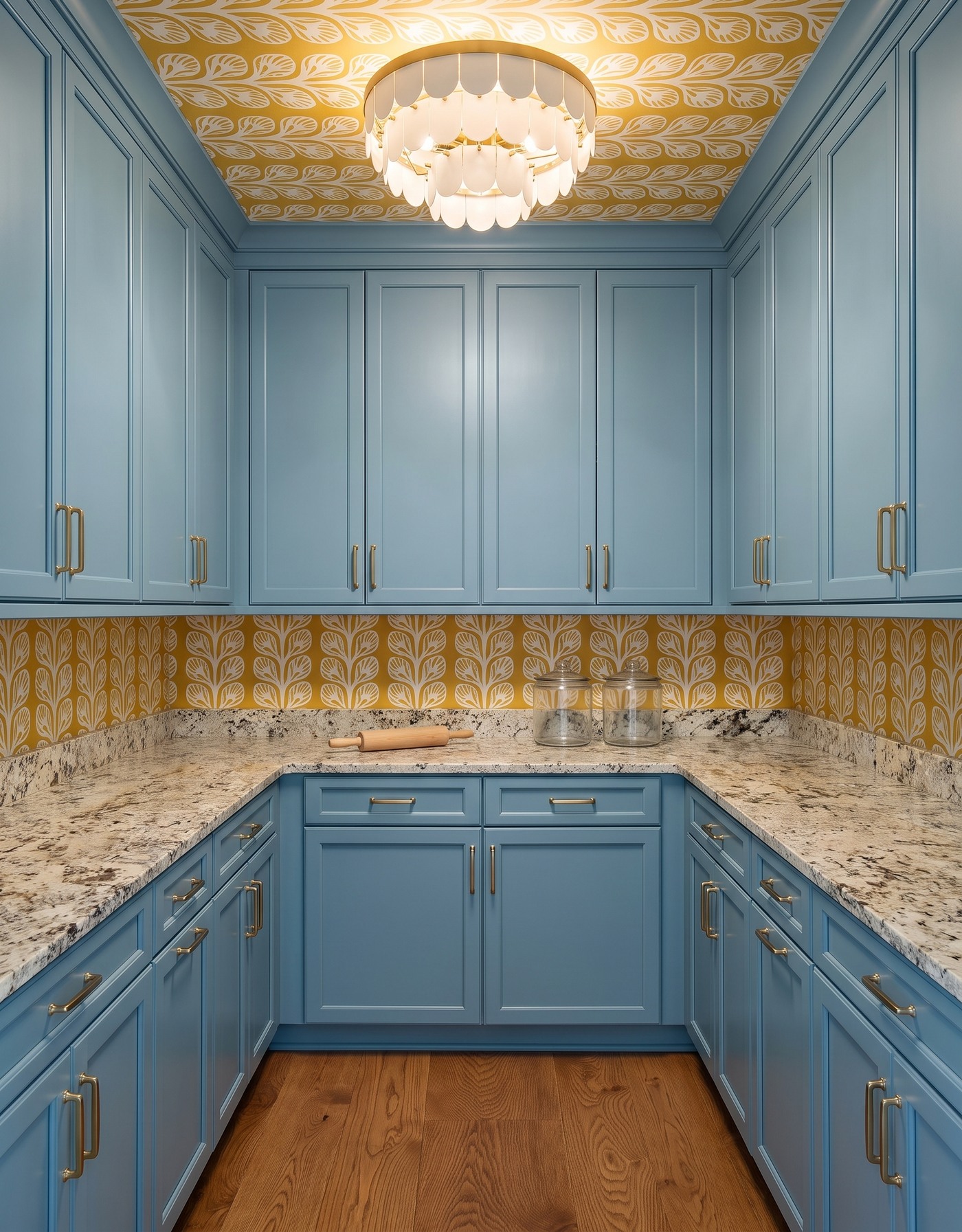 Pantry with muted blue cabinets, mustard-and-ivory leafy wallpaper, granular cream counter, warm wood floor and ivory petal light.