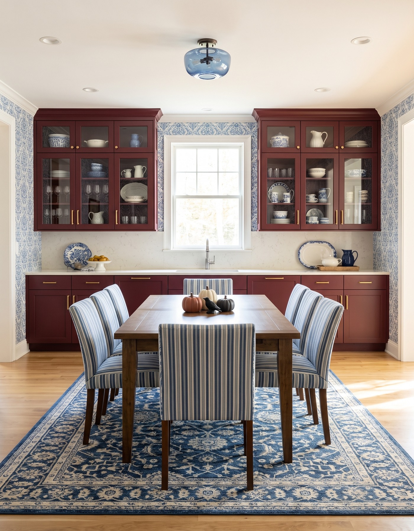 AI-created concept: Berry kitchen with blue leafy wallpaper, striped dining chairs and a small pumpkin-and-bird centerpiece.