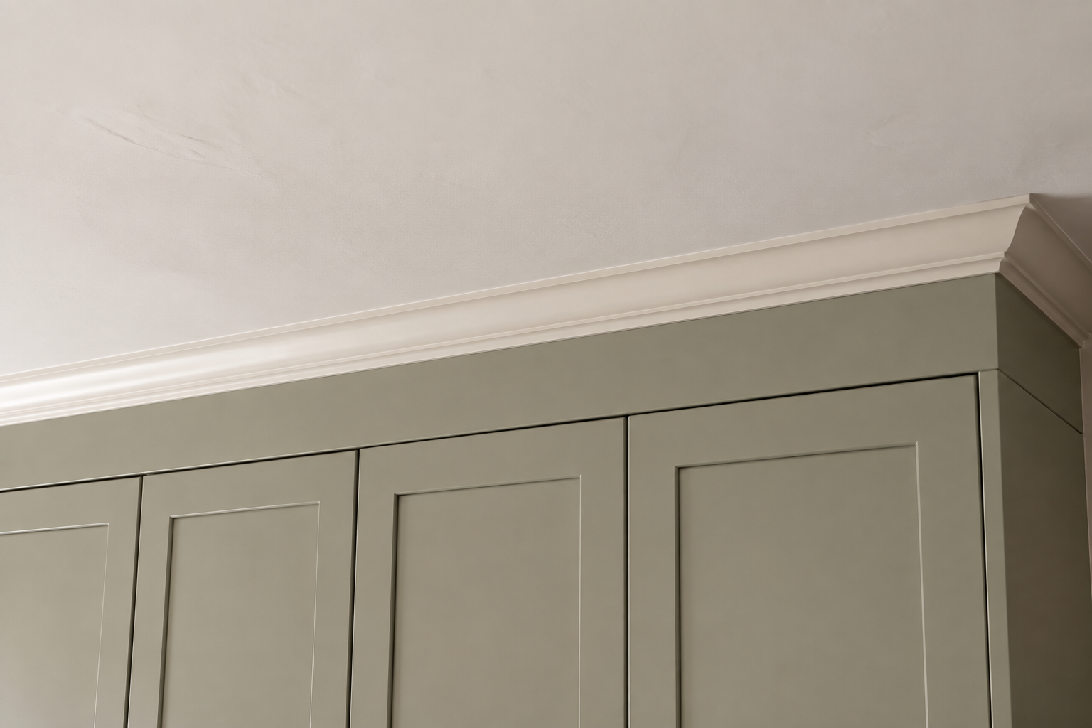 Simple crown molding and a straight fascia connect aligned sage cabinet doors to a slightly uneven plaster ceiling.