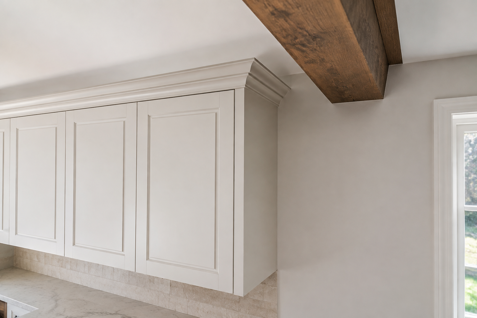 Warm-white cabinet crown ends with a clean return at a finished side panel before a large oak ceiling beam.