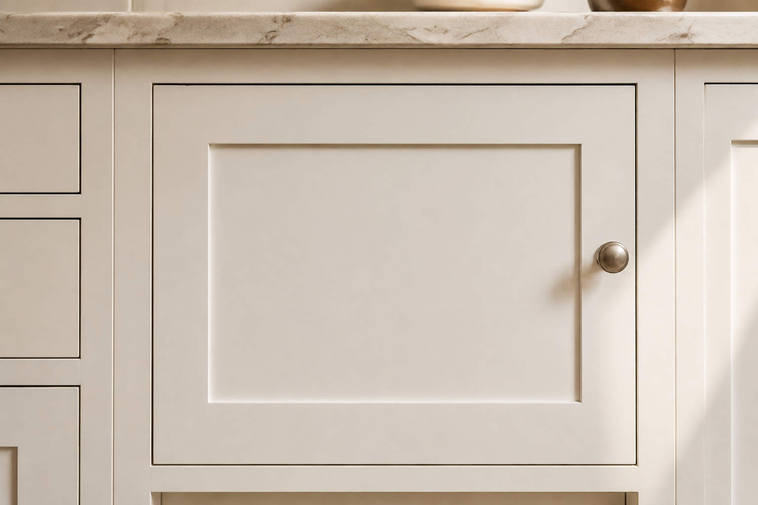 Close view of a closed warm-white painted five-piece solid cabinet door with a subtle hairline visible at one rail-and-stile joint.