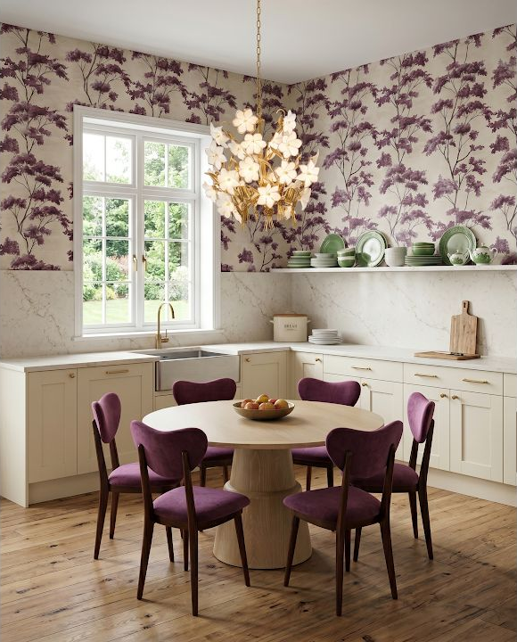 Concept image of a light kitchen with plum dining chairs, a round table, floral wallpaper, and a window.