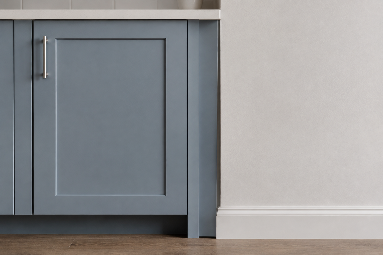 Closed muted-blue base cabinet separated from a plaster wall by a narrow fixed matching filler with no hardware.
