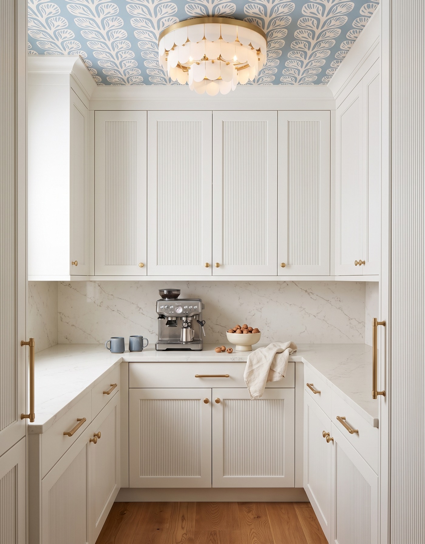 AI-created concept: White reeded pantry cabinetry frames blue leaf wallpaper, a cream tiered light and honey-toned flooring.