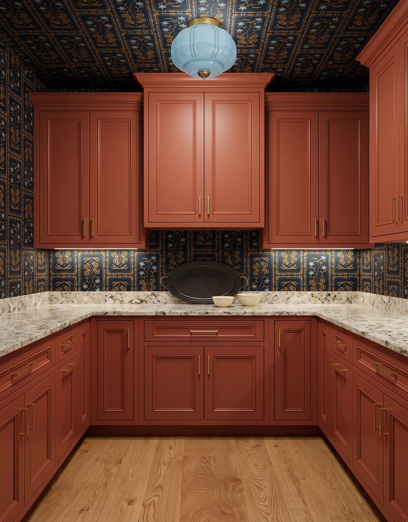Pantry with burnt orange raised-panel cabinets, navy-and-gold framed botanical wallpaper, pale densely speckled counters, golden wood floor and pale blue glass light.