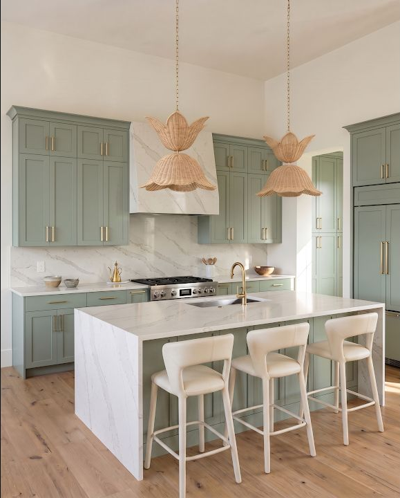 Concept image of a pale green kitchen with two woven pendant lights over an island and several white stools.