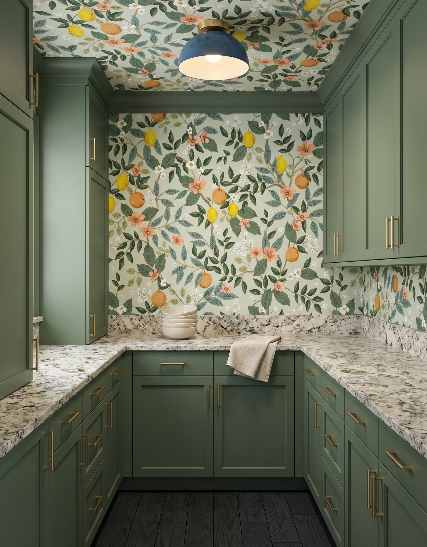Pantry with moss green cabinets, citrus-and-floral wallpaper, pale densely speckled counters, near-black wood floor and blue dome light.