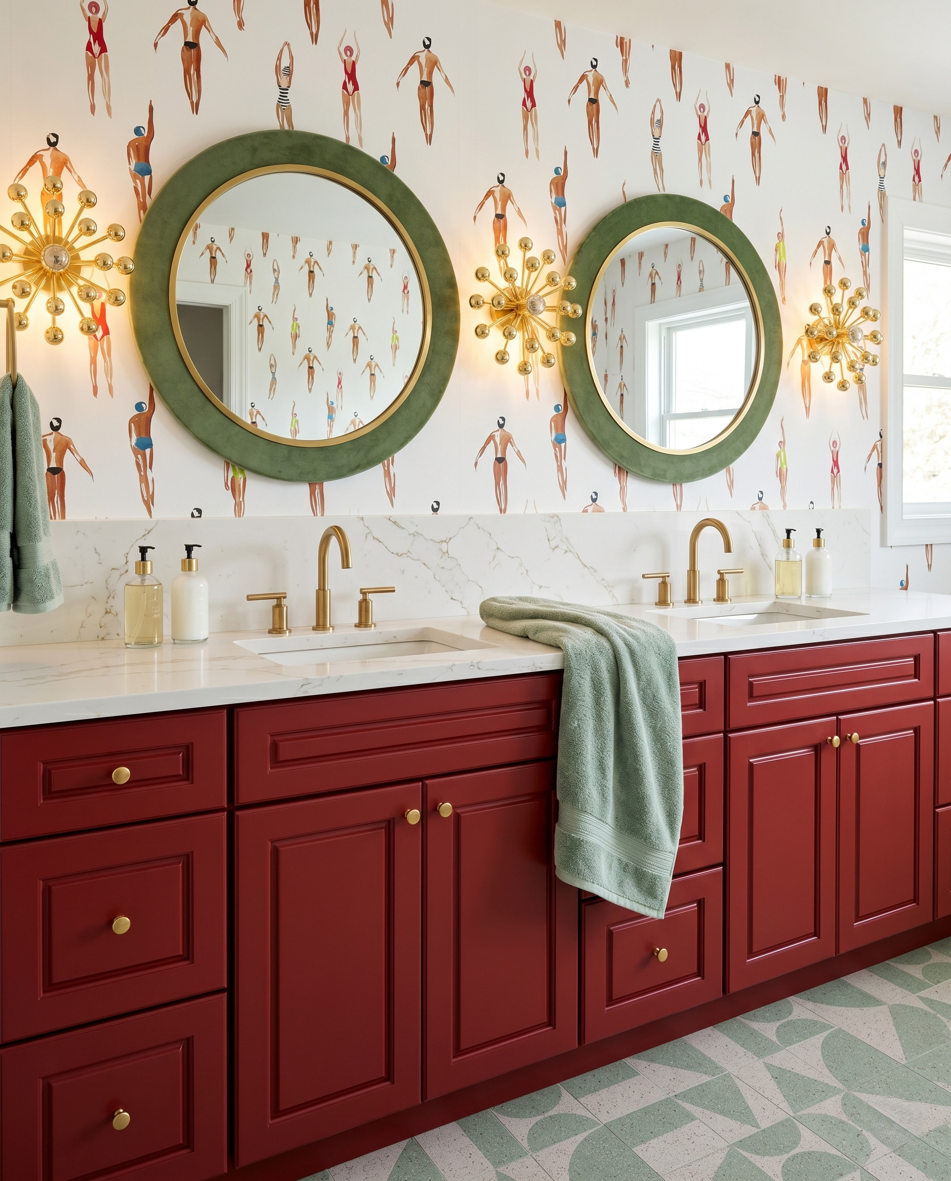 Barn-red double vanity with swimmer-print wallpaper, round green mirrors, brass starburst sconces and green patterned flooring.