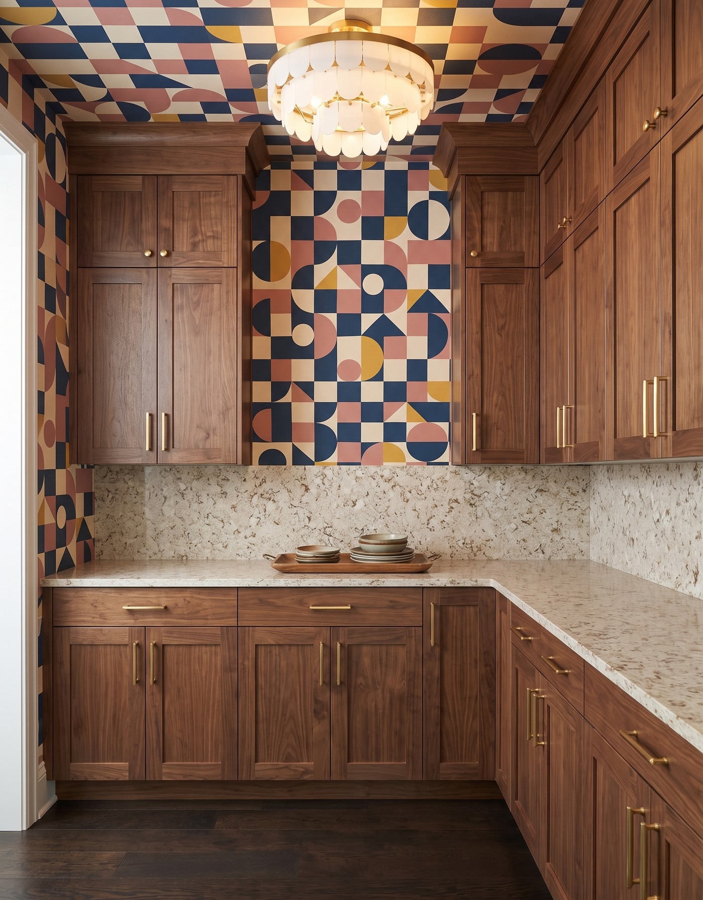 Pantry with walnut cabinets, navy-pink-mustard geometric wallpaper, warm mottled cream counters, dark brown wood floor and tiered ivory light.