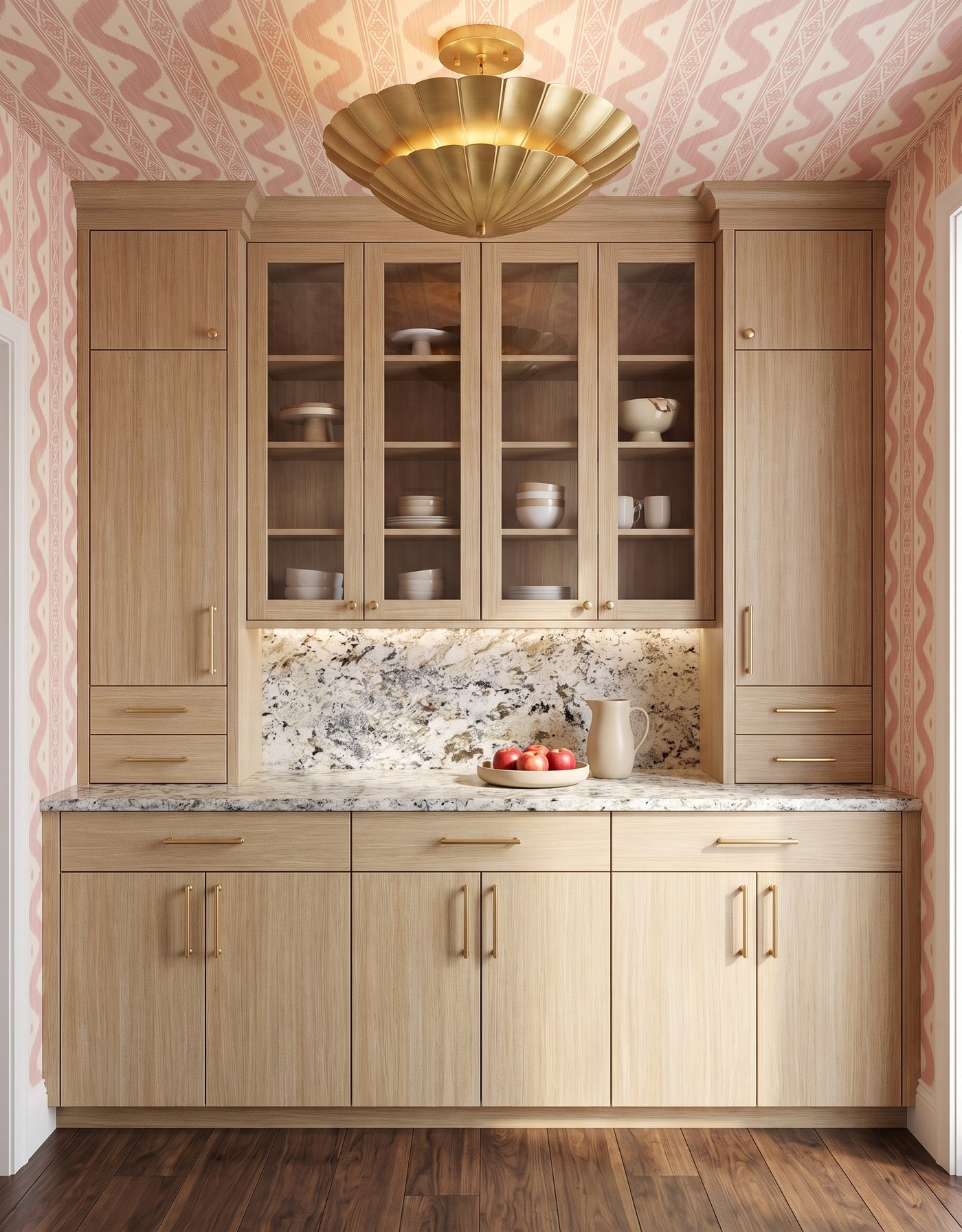 Pantry with pale oak cabinets with glazed upper doors, blush-and-ivory ikat wallpaper, pale densely speckled counters, warm brown wood floor and brass petal light.