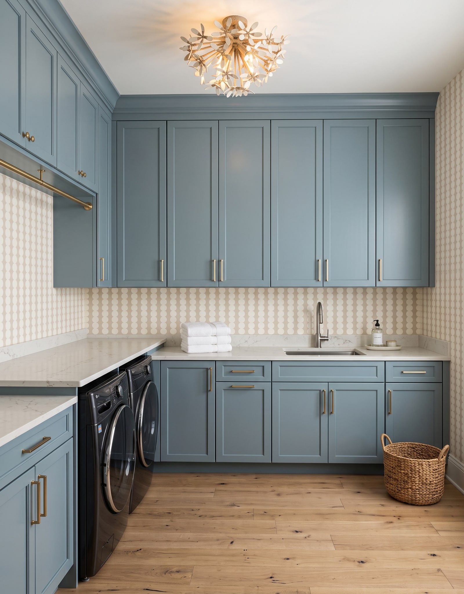 A light-blue laundry room with a front-load pair under an L-shaped counter, a sink wall, closed upper cabinets, and connections concealed behind the machines.