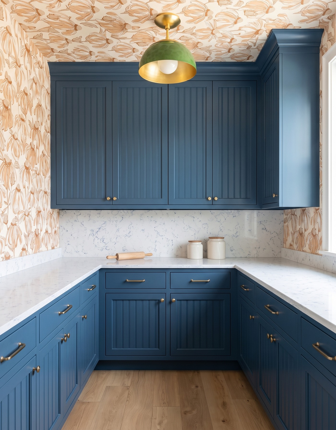 Pantry with denim blue beadboard cabinets, cream-and-camel outlined floral wallpaper, white fine blue-gray-veined counters, pale oak floor and green dome pendant.