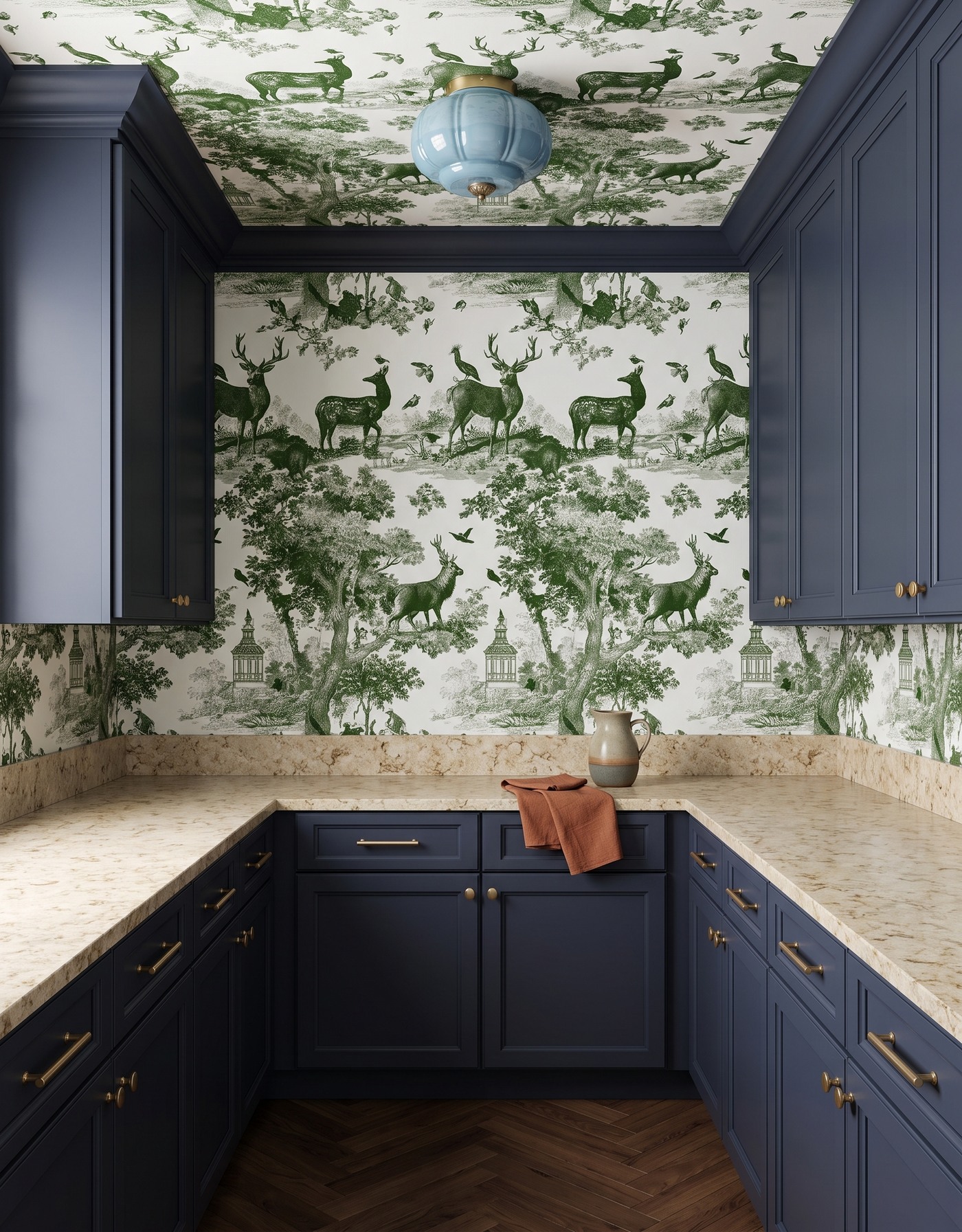 Pantry with slate navy cabinets, green-and-ivory woodland toile, warm mottled cream counters, brown herringbone floor and pale blue glass light.