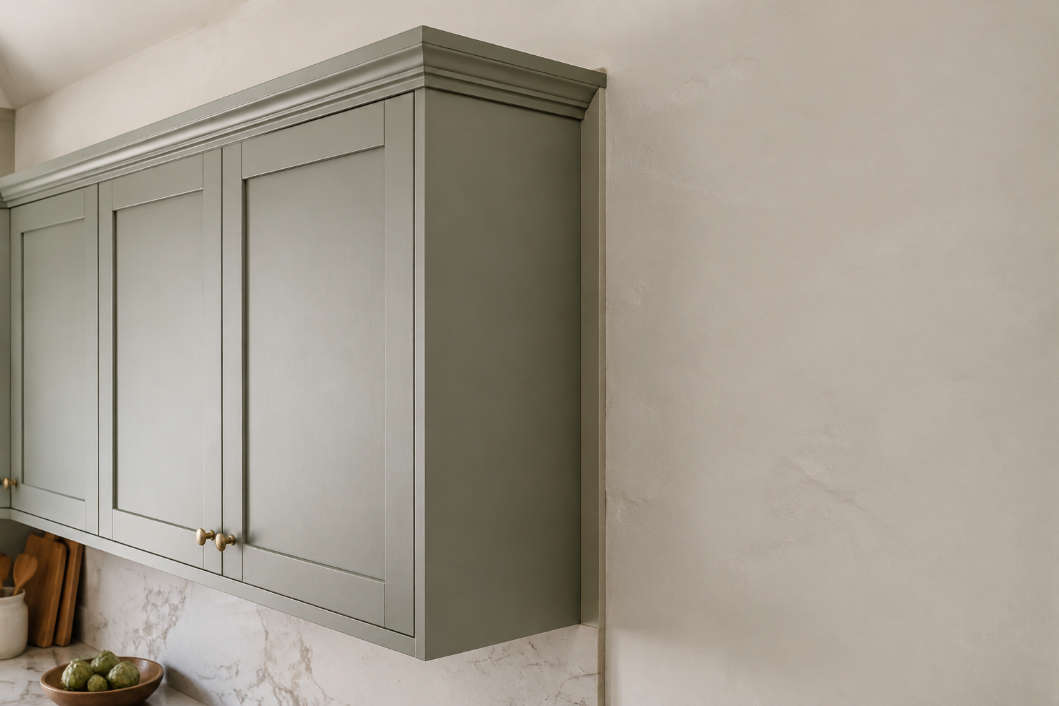 A complete sage wall-cabinet run uses a narrow scribe strip at the uneven plaster wall and returns crown neatly at the finished end.