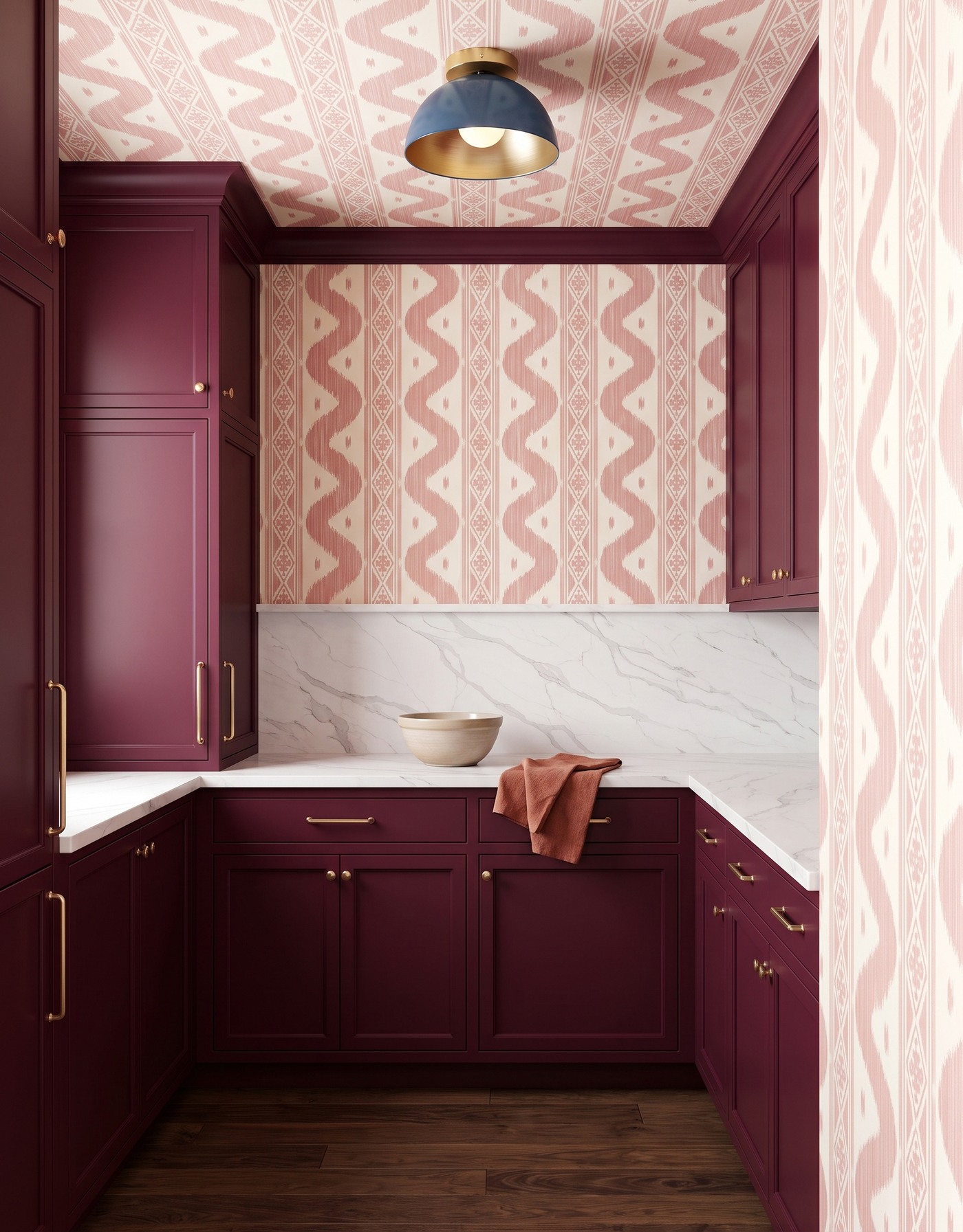 Pantry with burgundy cabinets, dusty pink-and-ivory ikat wallpaper, white diagonal gray-veined counter, dark wood floor and blue dome light.